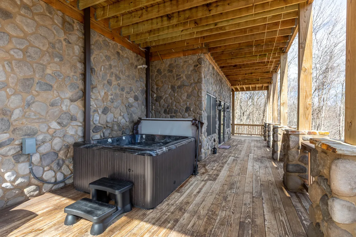 This image features an outdoor hot tub set against stone walls and wooden beams on a spacious deck. Surrounded by the serene outdoors, it provides a peaceful spot for soaking while enjoying the sights and sounds of nature. The space is ideal for unwinding after a day of exploring local attractions.