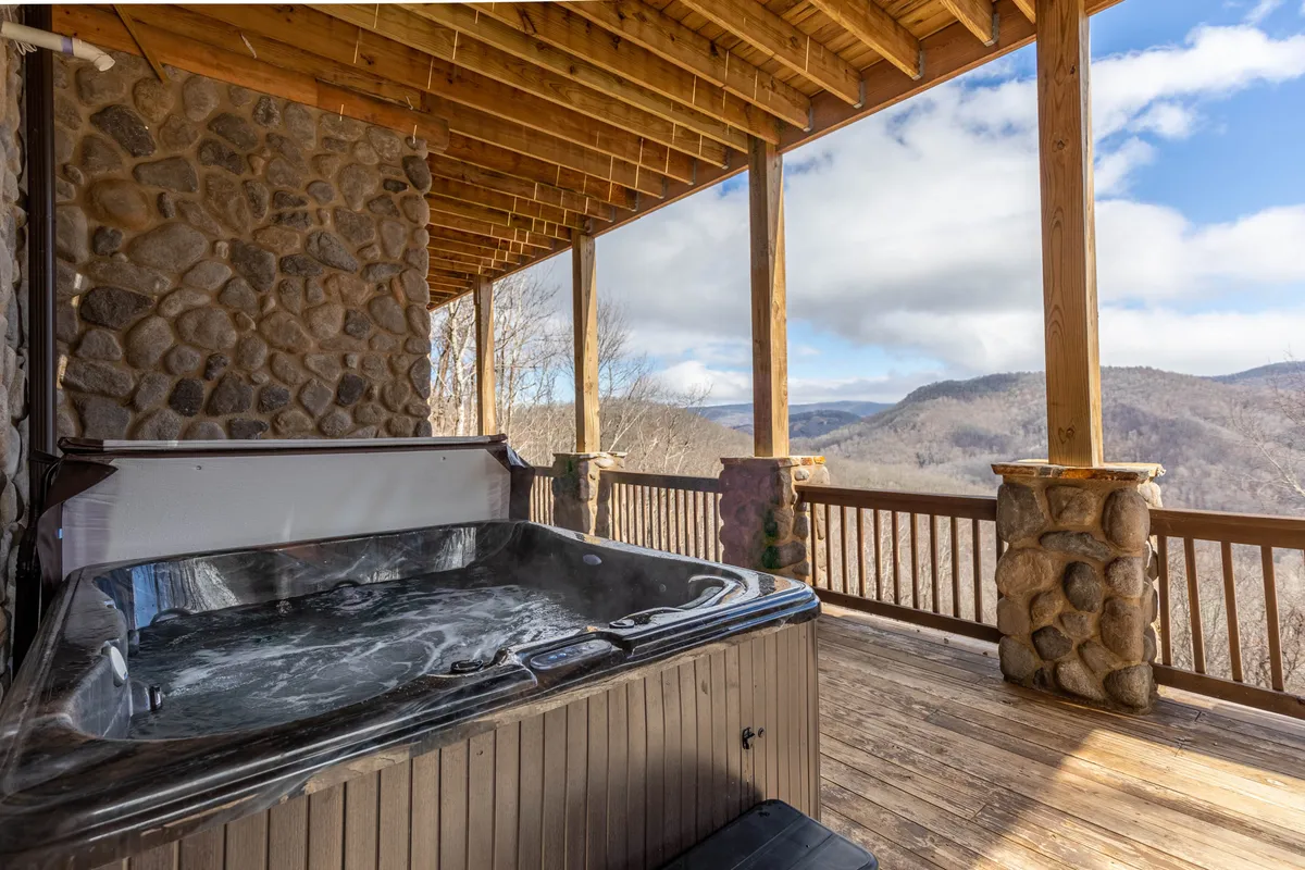A tranquil exterior deck with a hot tub, stone columns, and spectacular sunrise mountain views. The scene is inviting, blending relaxation with a strong connection to the outdoors.