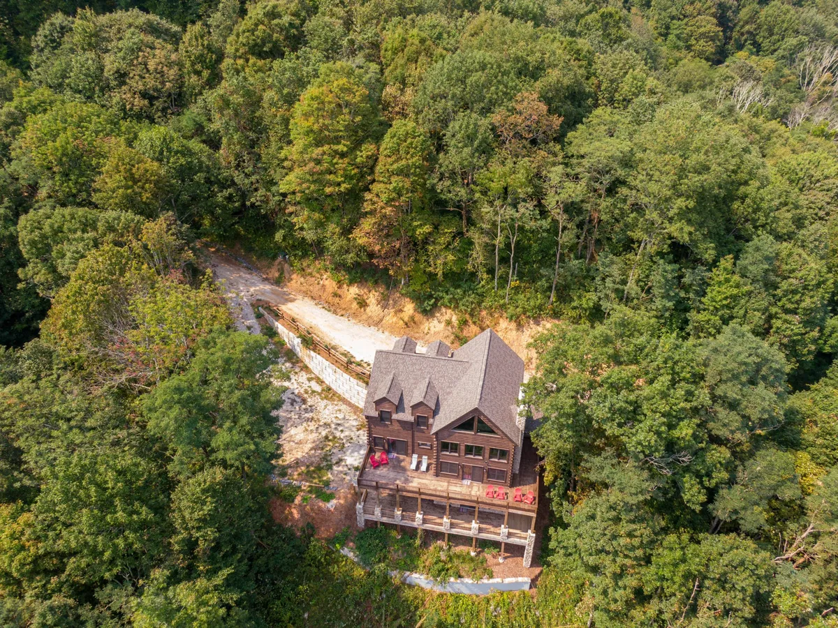 This image captures a wide view of the lodge, its spacious deck, and the surrounding forested landscape. The vantage point shows the lodge nestled in nature, with ample outdoor space for gatherings, morning coffee, or sunset appreciation. The peaceful setting underscores the sense of privacy and escape.