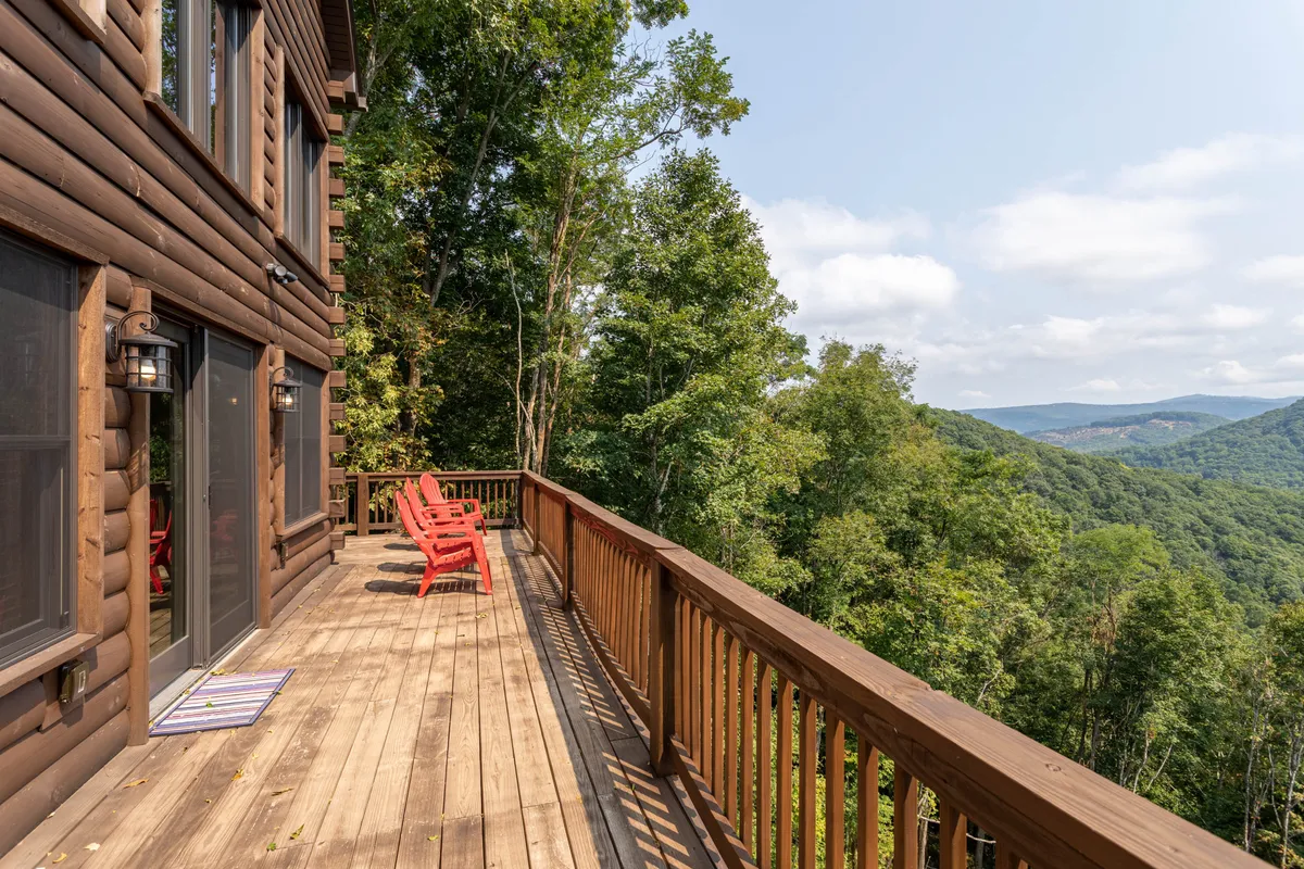 This image shows a peaceful wooden deck furnished with vibrant red Adirondack chairs, overlooking a stunning mountain vista. The deck is elevated, providing an unobstructed view across the treetops to the distant peaks, with plenty of space to relax and enjoy the scenery.