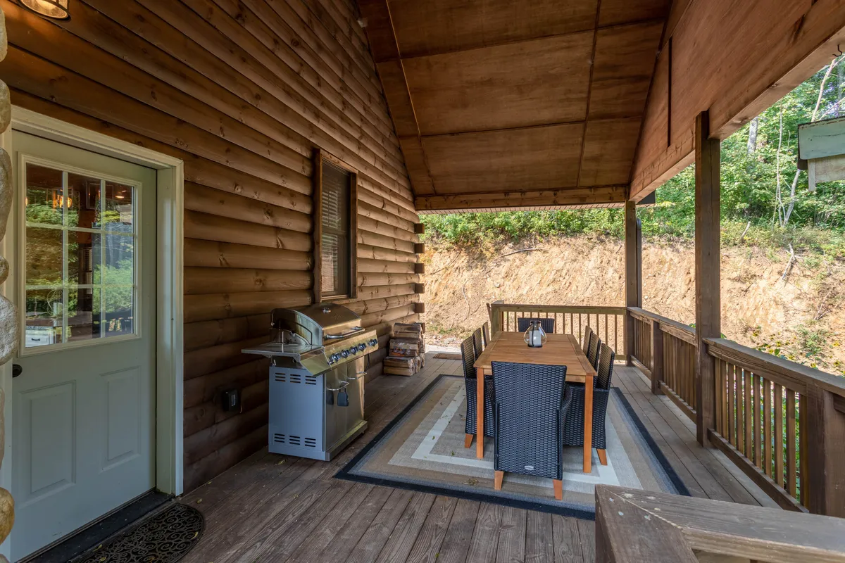 A cozy covered outdoor dining area featuring a grill, spacious table, and decorative rug, all set against rustic wooden walls. The setup invites guests to gather for alfresco meals or festive barbecue evenings while staying sheltered and comfortable.