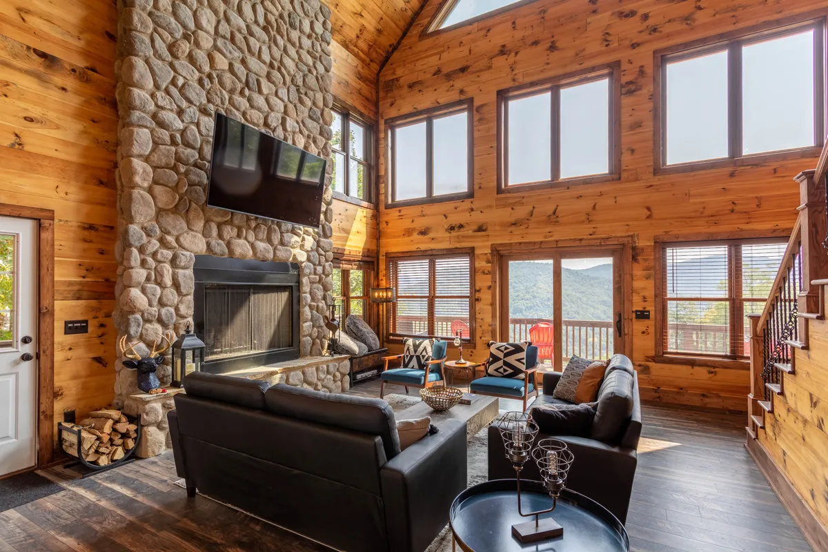 A cozy, inviting interior space featuring a prominent stone fireplace, comfortable seating arranged for groups, and large windows that flood the room with natural light. The arrangement hints at a relaxed, social atmosphere—perfect for gatherings, games, or enjoying the view.