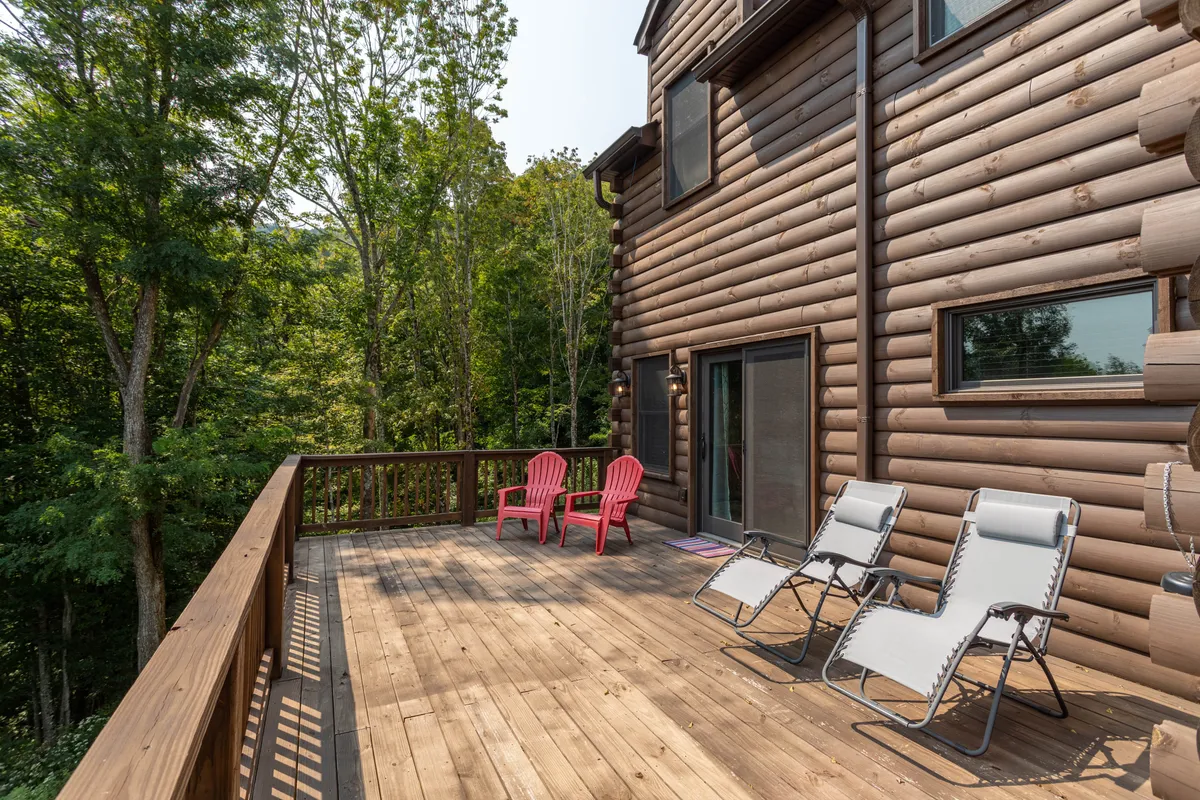 An exterior wooden deck featuring red and lounge chairs surrounded by trees. The deck is accessible and inviting, connected directly to the outdoors, suggesting a seamless transition from inside entertainment to fresh-air relaxation.