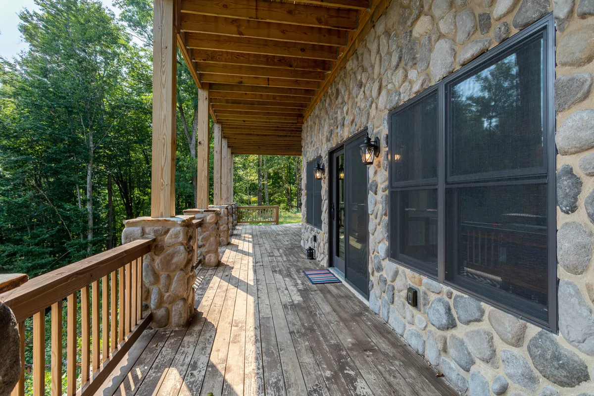 This image displays a charming wooden deck with stone walls and screened doors, accented by lantern lighting. The space is surrounded by lush greenery, evoking a tranquil mountain retreat atmosphere, and is clearly designed for outdoor relaxation and enjoying the natural surroundings.