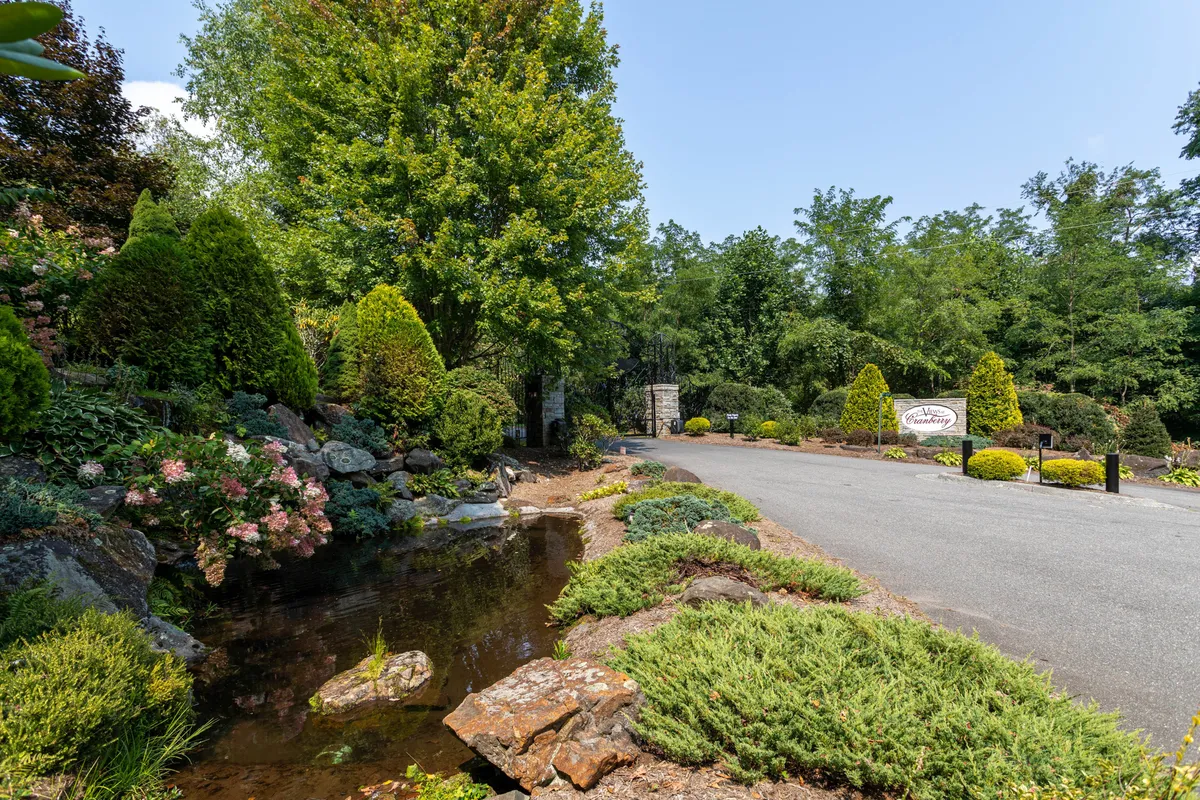 A scenic outdoor view featuring lush greenery, a tranquil water feature, a stone pathway, and a welcoming entrance sign. The landscape is vibrant and photogenic, inviting exploration and outdoor enjoyment.